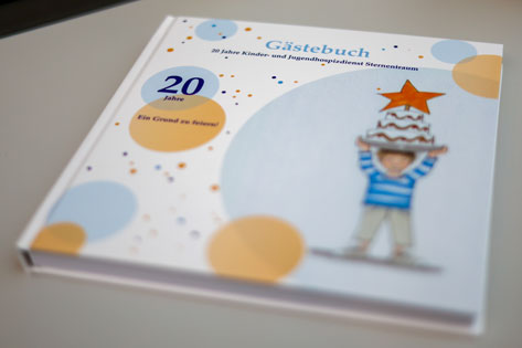 Das Bild zeigt ein Gästebuch für das 20-jährige Jubiläum des Kinder- und Jugendhospizdienstes Sternentraum. Auf dem Cover ist eine Illustration eines Kindes zu sehen, das eine Torte mit einem Stern darauf trägt.