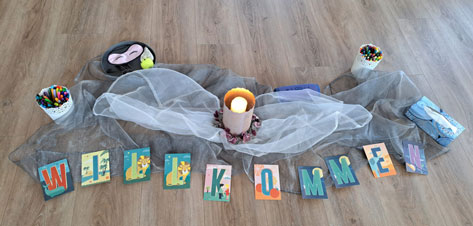 Erika-Elmer-Stiftung Das Bild zeigt eine Dekoration auf einem Holzboden. Im Vordergrund liegen Karten, die zusammen das Wort