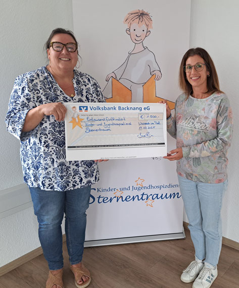 Das Bild zeigt zwei Frauen, die einen symbolischen Scheck der Volksbank Backnang eG in Höhe von 2.500 Euro an das Kinder- und Jugendhospiz Sternentraum übergeben. Die Übergabe findet vor einem Roll-up mit dem Logo des Hospizes und einer kindlichen Illustration statt. Die Stimmung ist positiv und feierlich. Das Foto dokumentiert eine Spendenübergabe und die damit verbundene Unterstützung einer wohltätigen Einrichtung.