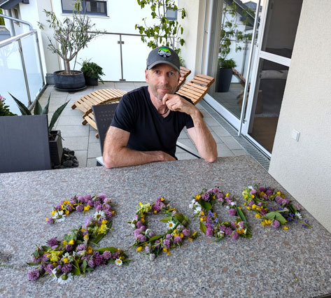 Mann sitzt auf einem Balkon, vor ihm auf dem Tisch ist die Zahl 2000 in Blumen ausgelegt