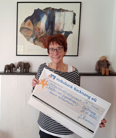Das Bild zeigt eine Frau mittleren Alters, die lächelnd in die Kamera schaut und einen übergroßen Scheck der Volksbank Backnang eG mit einer Spende von 3500 Euro hält. Der Scheck ist für den 