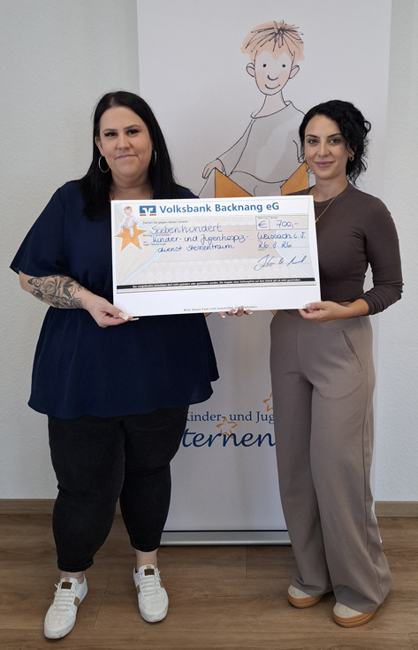 2 Frauen halten einen Scheck über 700 Euro und stehen vor einem Banner mit einem Sternenkind drauf.