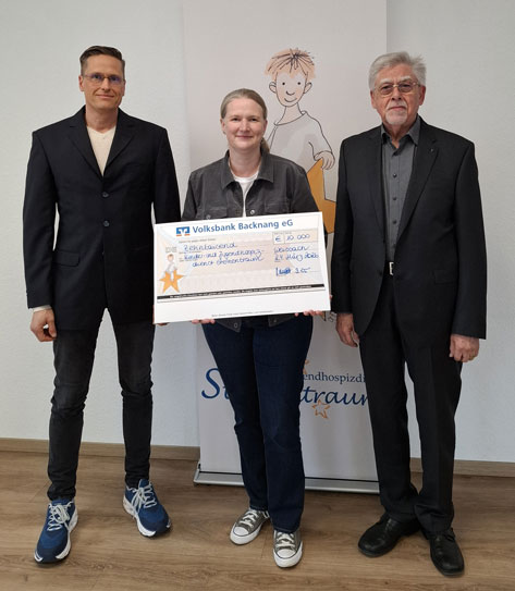 SCHLOTT Feuerschutz Drei Personen stehen nebeneinander und halten einen großen Scheck. Hinter ihnen ist eine kindliche Zeichnung eines Jungen und ein Banner mit der Aufschrift