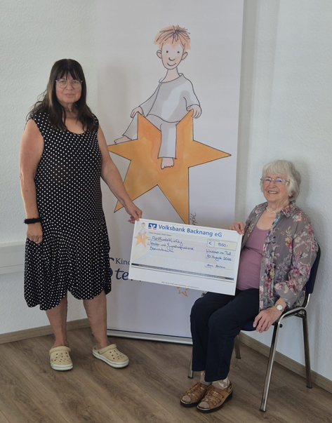 Zwei Frauen halten einen Scheck, der Volksbank Backnang eG, über 850 Euro. Im Hintergrund ist ein Banner mit einem gezeichneten Sternenkind zu sehen.